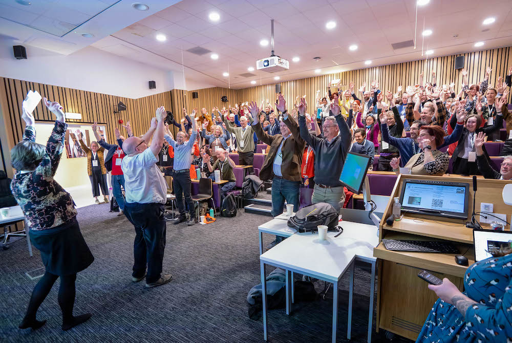 Photo of the OER23 Conference audience raising their arms