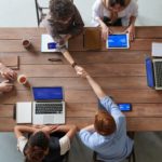 People working around a table with devices and two of them are shaking hands